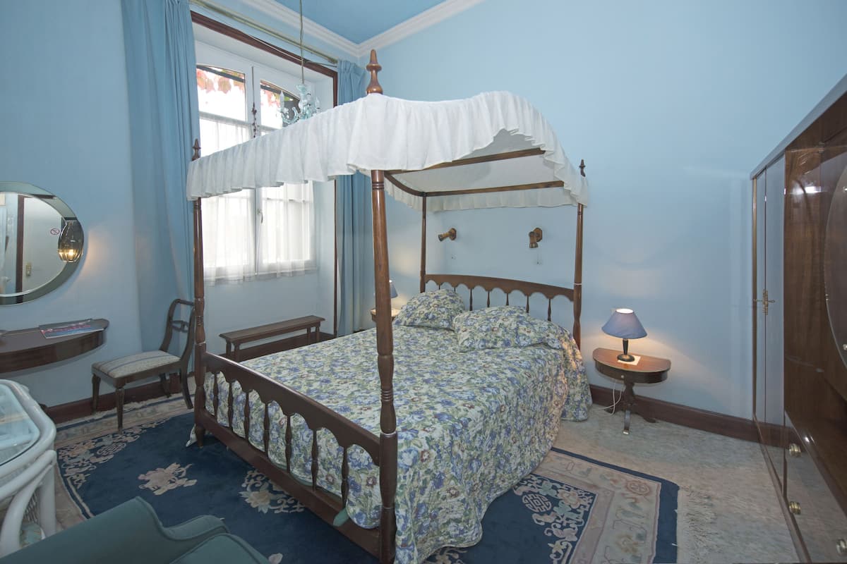 A four-poster bed with a canopy, a bedside table with a lamp, a chair, and a mirror on the wall.