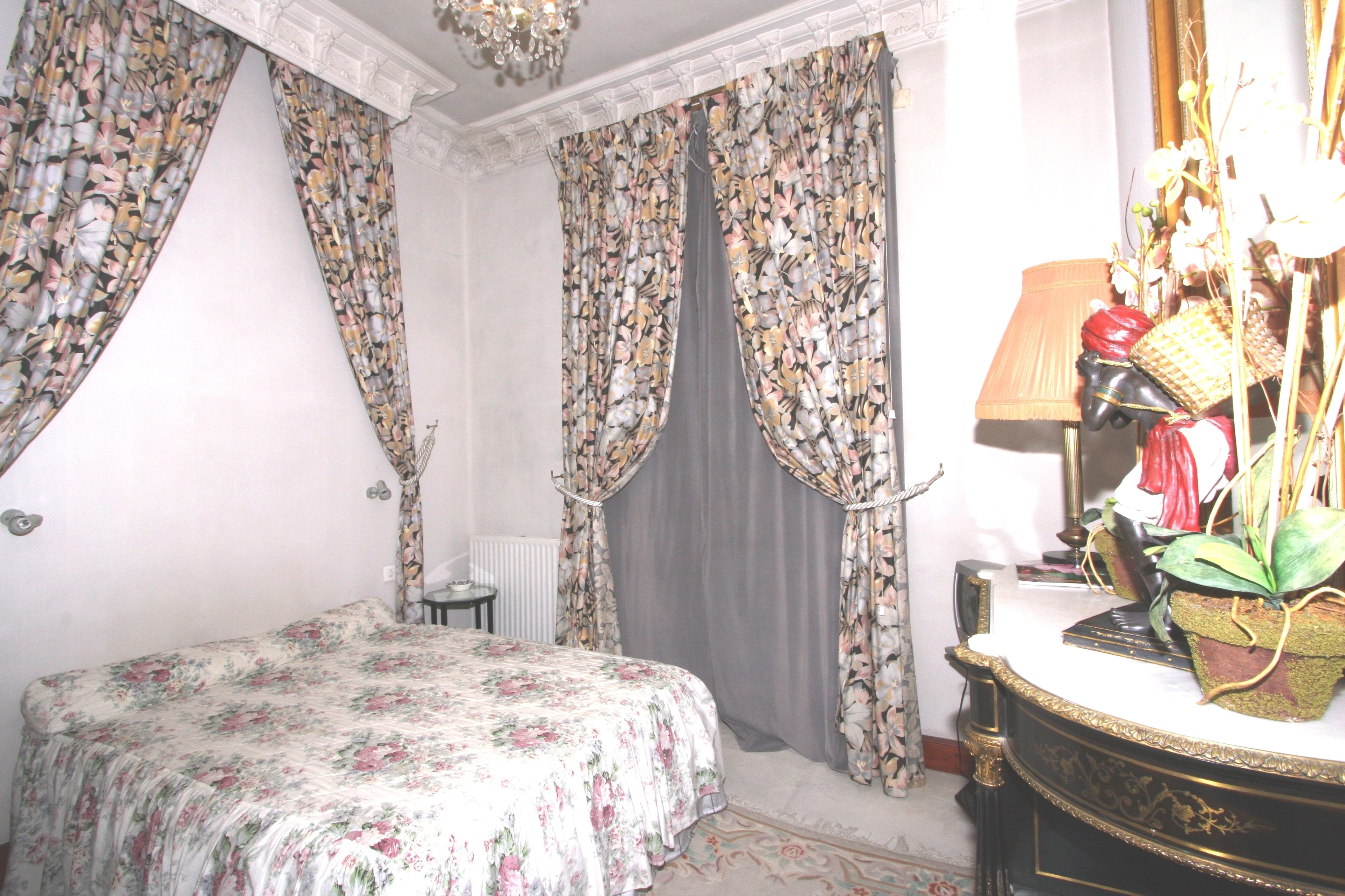 Un dormitorio con colcha floral, cómoda con objetos decorativos y cortinas con estampado de flores.