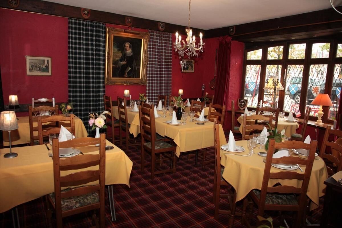 A dining area with multiple tables set for service, wooden chairs, and a red carpeted floor.