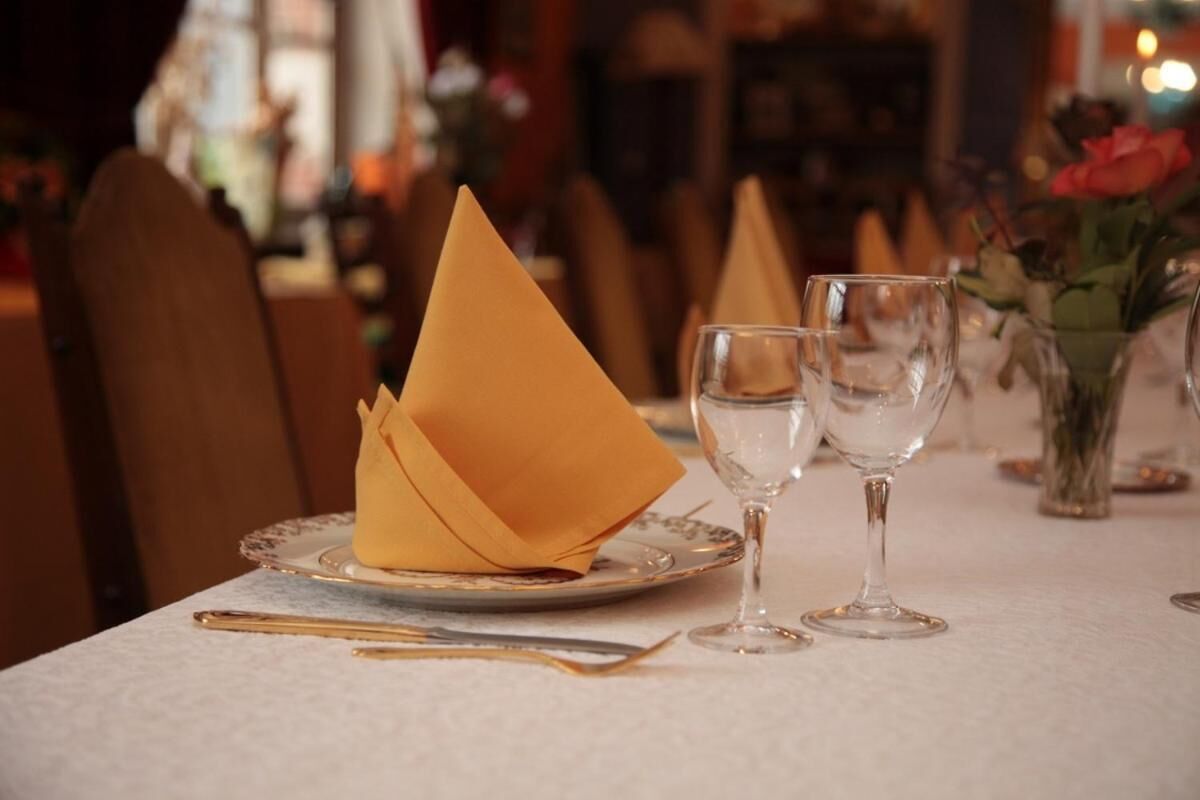 Una mesa de comedor preparada con un servilleta doblada, dos copas de vino y un juego de cubiertos dorados.