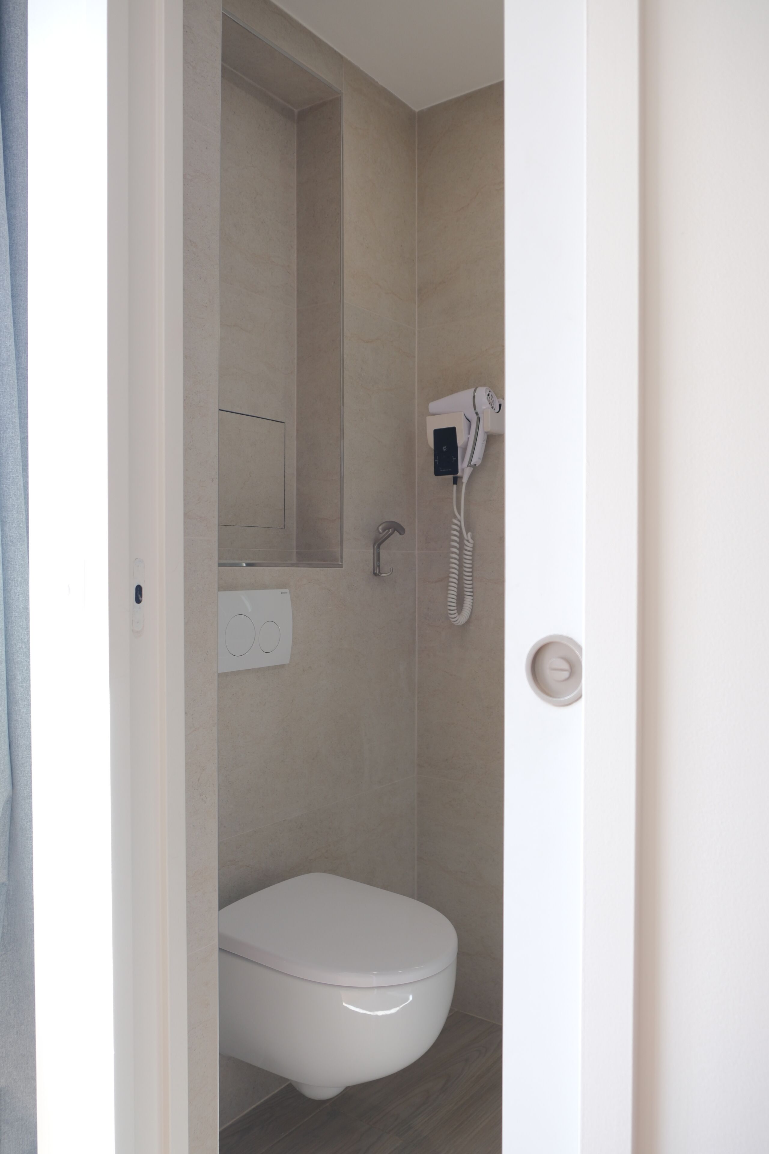 A bathroom with a toilet, a mirror, a hairdryer, and a wall-mounted light switch.