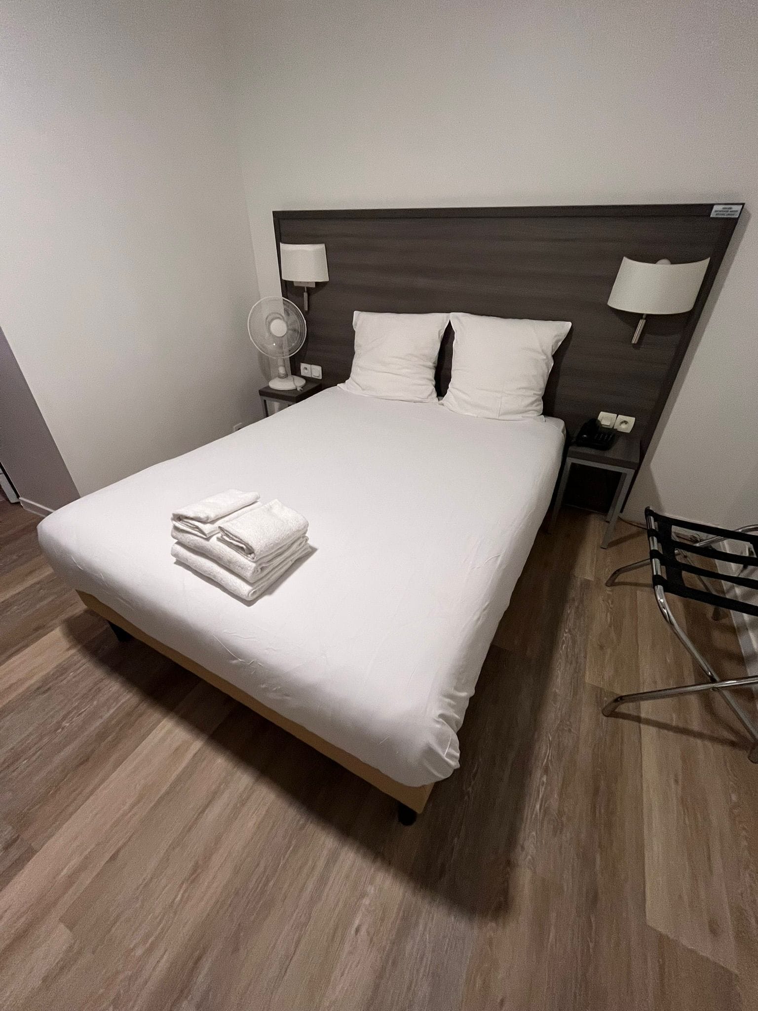 Una cama bien tendida con sábanas blancas y una toalla doblada al pie.