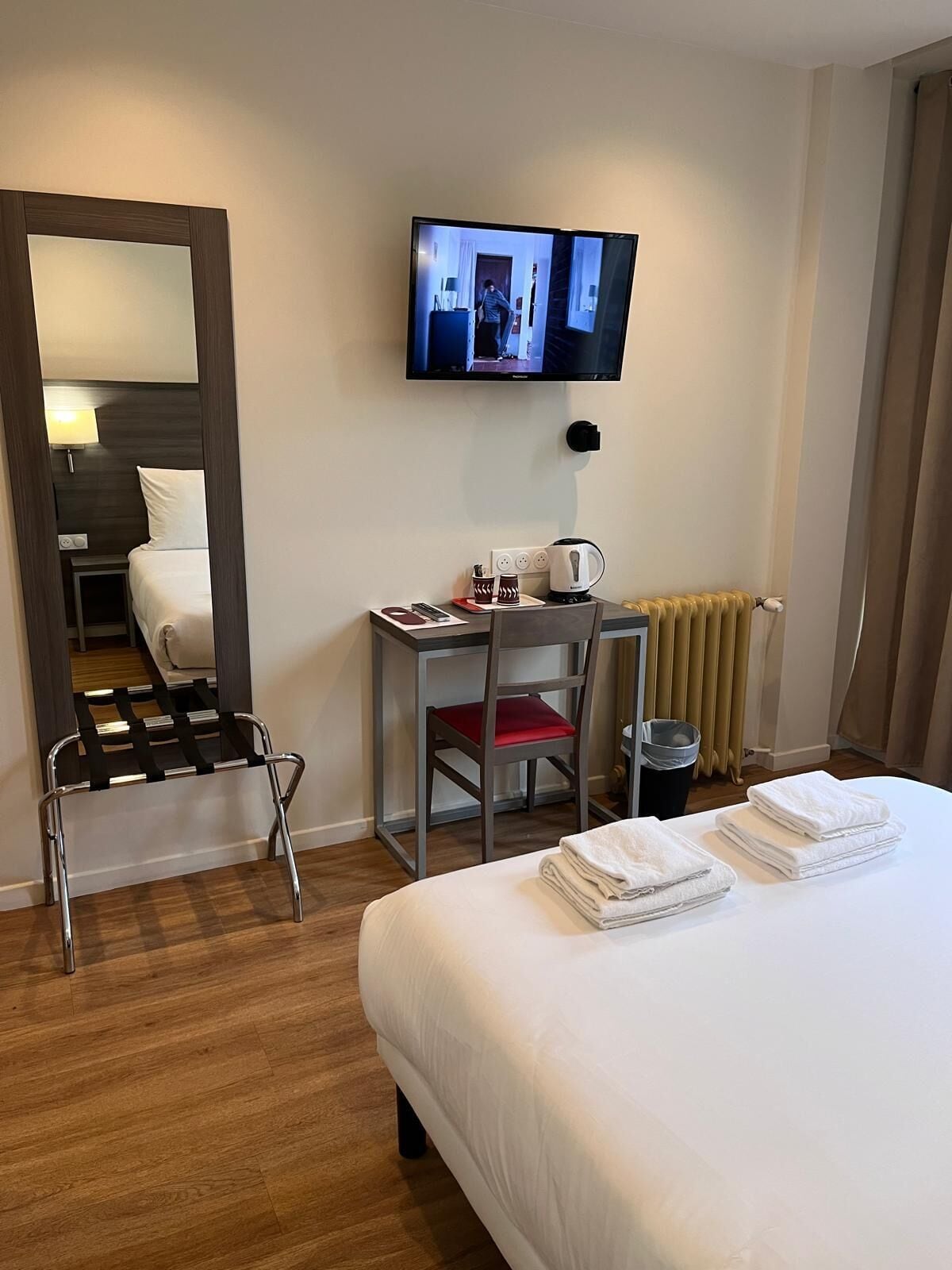 Hotellihuone, jossa on sänky, työpöytä tuolilla, seinälle asennettu televisio ja patteri.