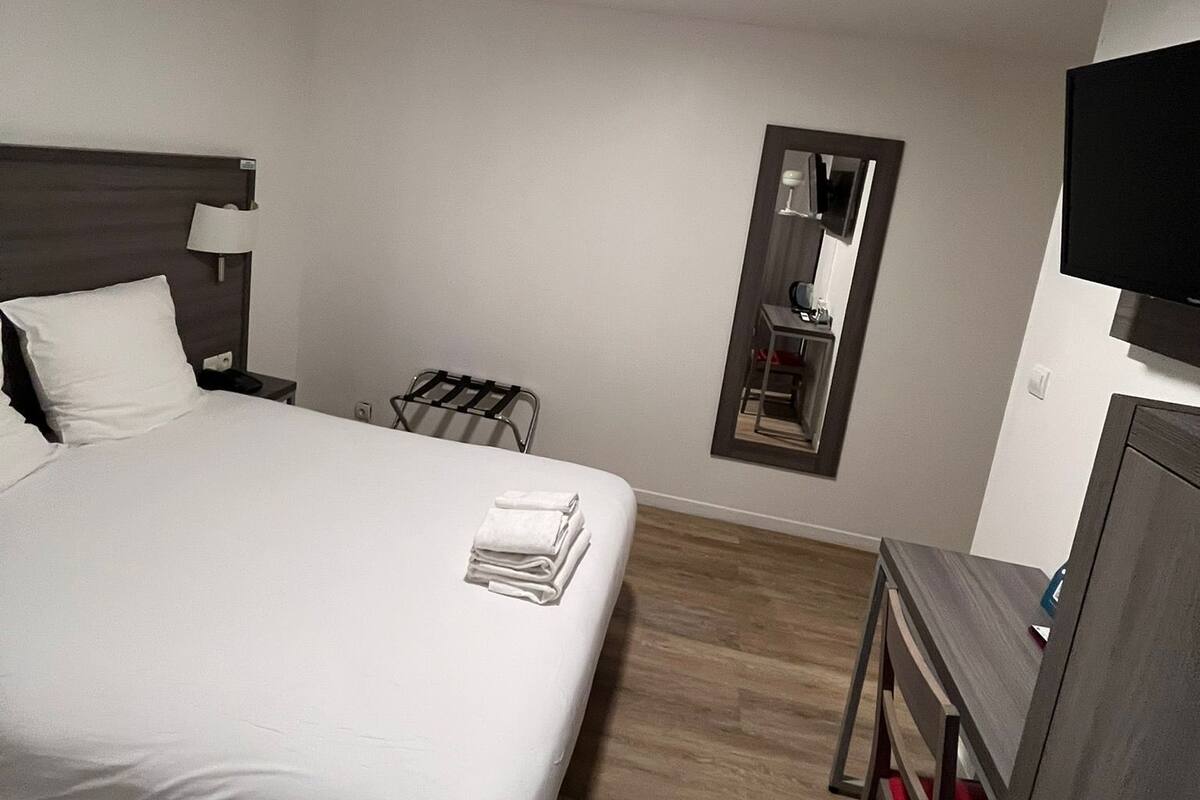 Een hotelkamer met een bed, een bureau, een stoel, een televisie, een spiegel en een tafeltje met een lamp.