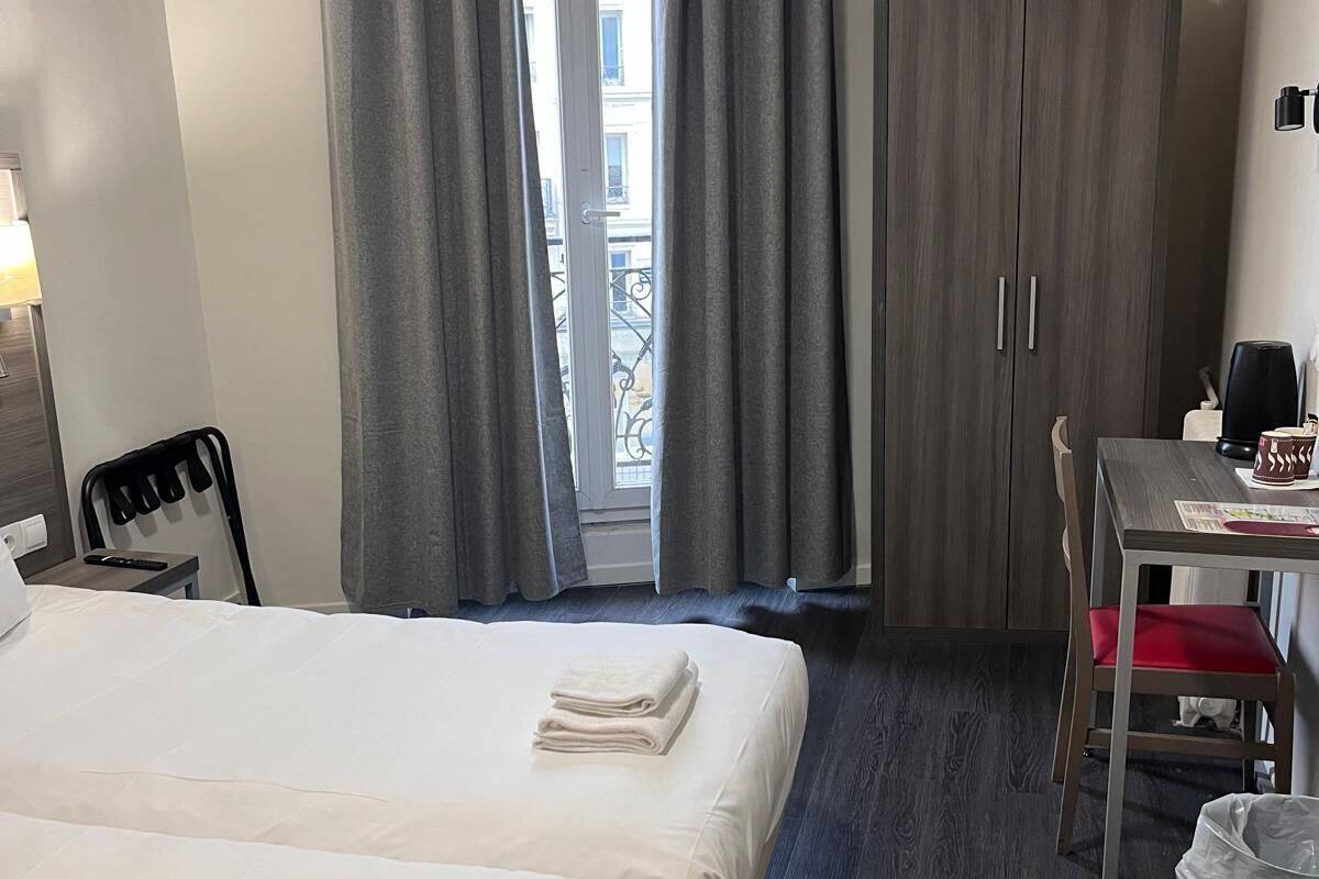 Een hotelkamer met twee bedden, een bureau met stoel, een kledingkast en een raam met gordijnen.