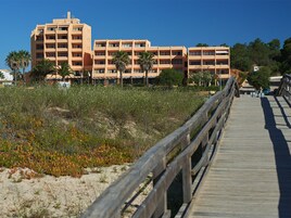 A wooden boardwalk leading to a multi-story hotel with balconies and a landscaped garden.
