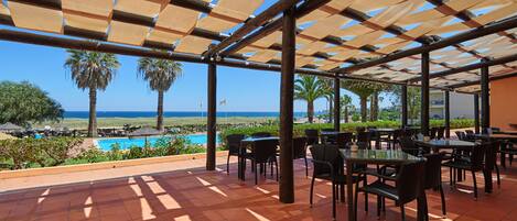 An outdoor patio with tables and chairs, overlooking a pool and the ocean.
