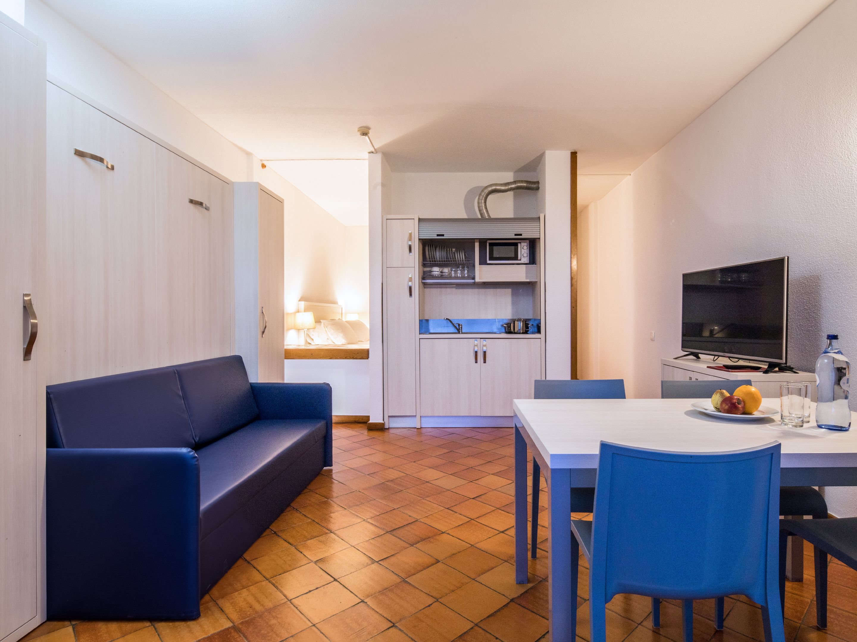 A compact living space with a sofa, a dining table with chairs, a kitchenette, and a television.