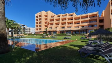 Een hotel met een zwembad, ligbedden en een palmboom.