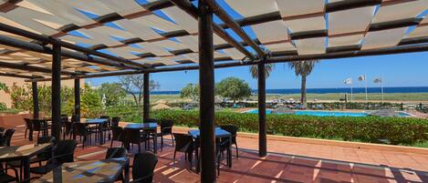 An outdoor patio with tables and chairs, a pool, and a view of the ocean.