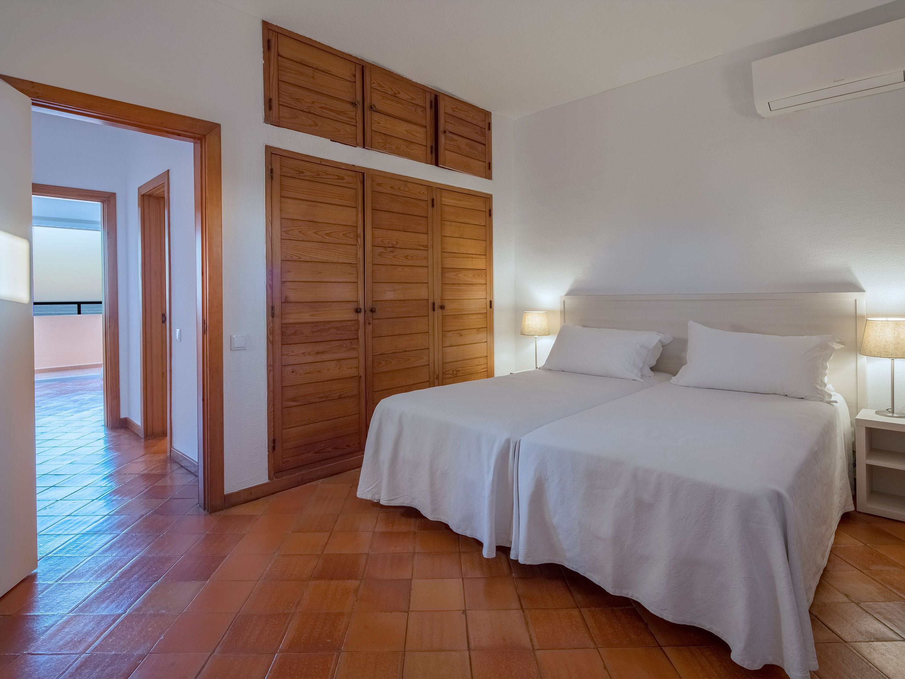 Une chambre avec deux lits, des armoires en bois, une table de chevet et un appareil de climatisation.