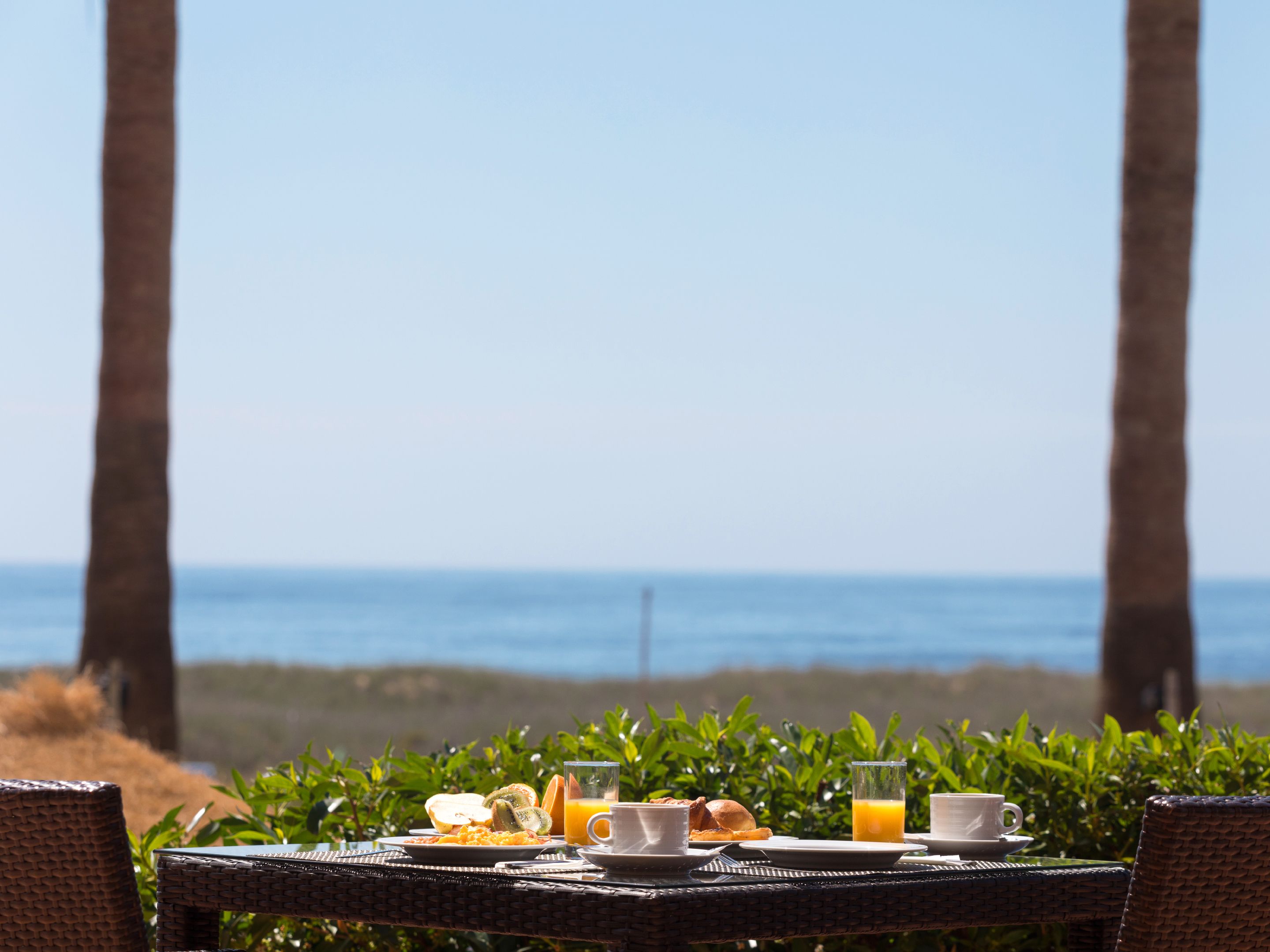 A breakfast table with plates of food, glasses of orange juice, and a view of the ocean.