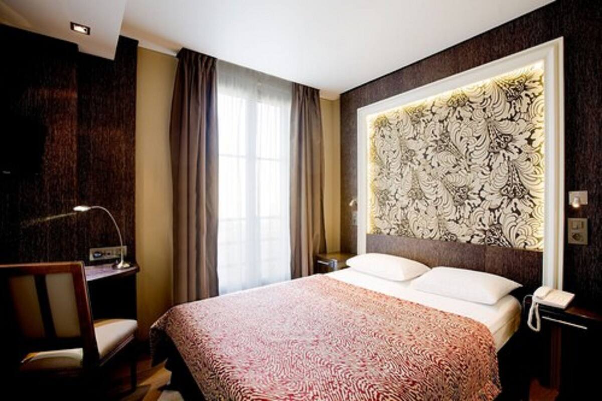 Une chambre d’hôtel avec un grand lit, un bureau avec une lampe, une chaise et un panneau décoratif au mur.