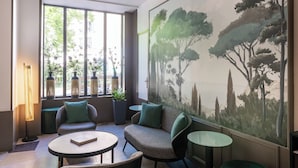 Zona d'estar moderna amb un sofà, dues taules petites i un gran finestral amb vista a arbres i edificis.