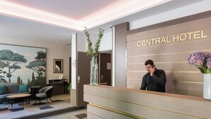 Un taulell de recepció d'hotel amb un disseny modern, un quadre gran amb arbres i una zona de seients amb un sofà i cadires.