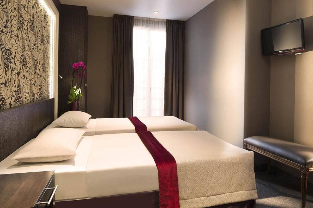 Une chambre d’hôtel avec deux lits, un banc, une télévision et une fenêtre avec des rideaux.