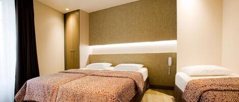 A hotel room with two beds, a headboard with built-in lighting, and a bedside telephone.