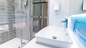 A modern bathroom with a glass-enclosed shower, a white sink with a blue faucet, and a tiled wall.