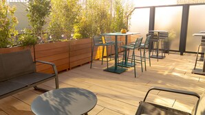 An outdoor patio with wooden flooring, metal chairs, a round table, and a bench.