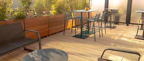 Un patio al aire libre con suelo de madera, sillas de metal, una mesa redonda y un banco.