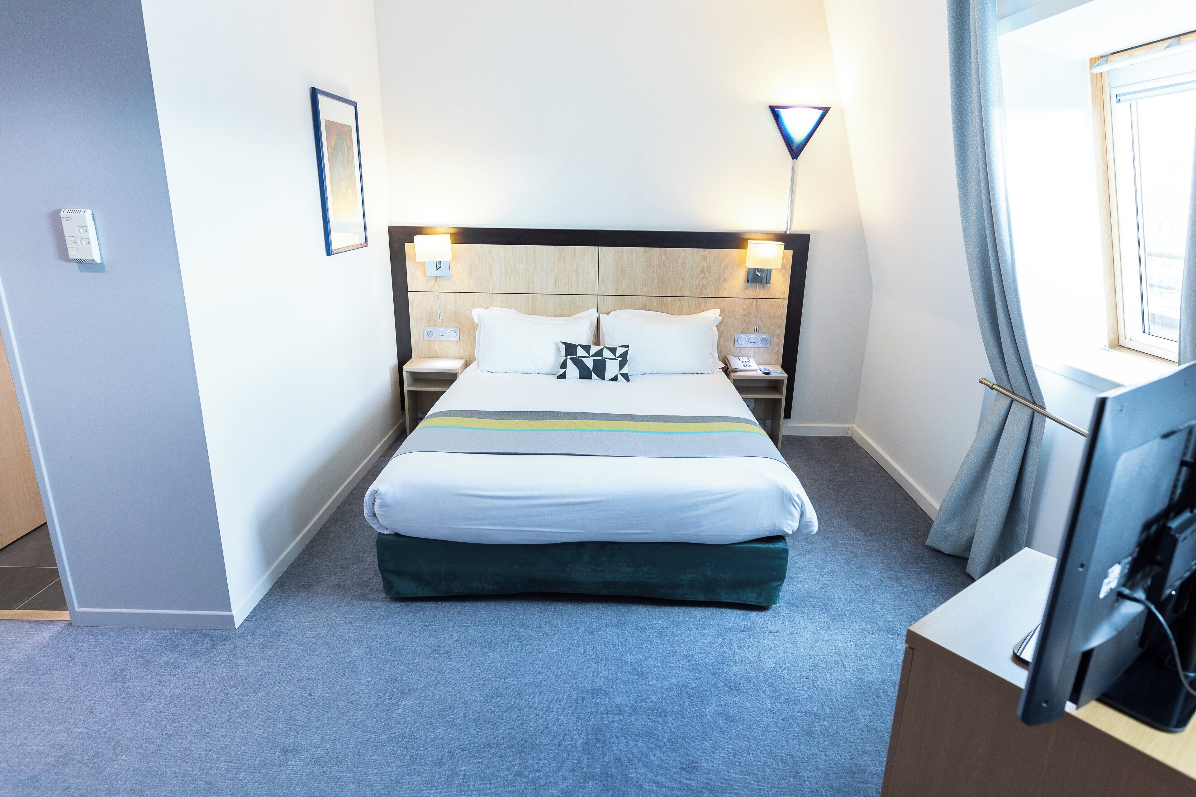 A hotel room with a bed, bedside tables, a TV, and a lamp.