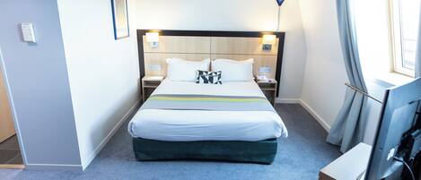 A hotel room with a bed, bedside tables, a TV, and a lamp.
