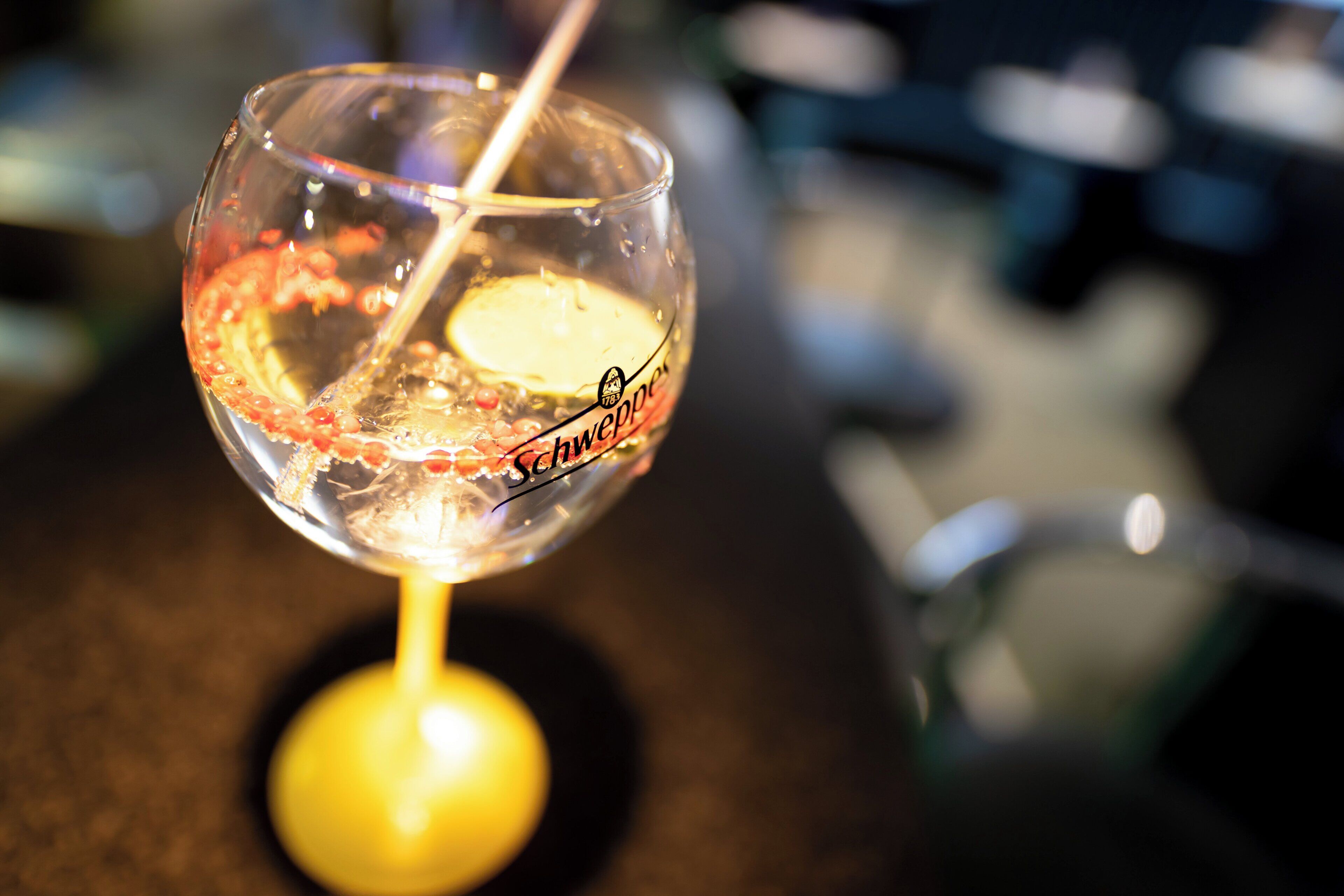 A clear glass with a straw, possibly containing a beverage, on a surface with a blurred background.