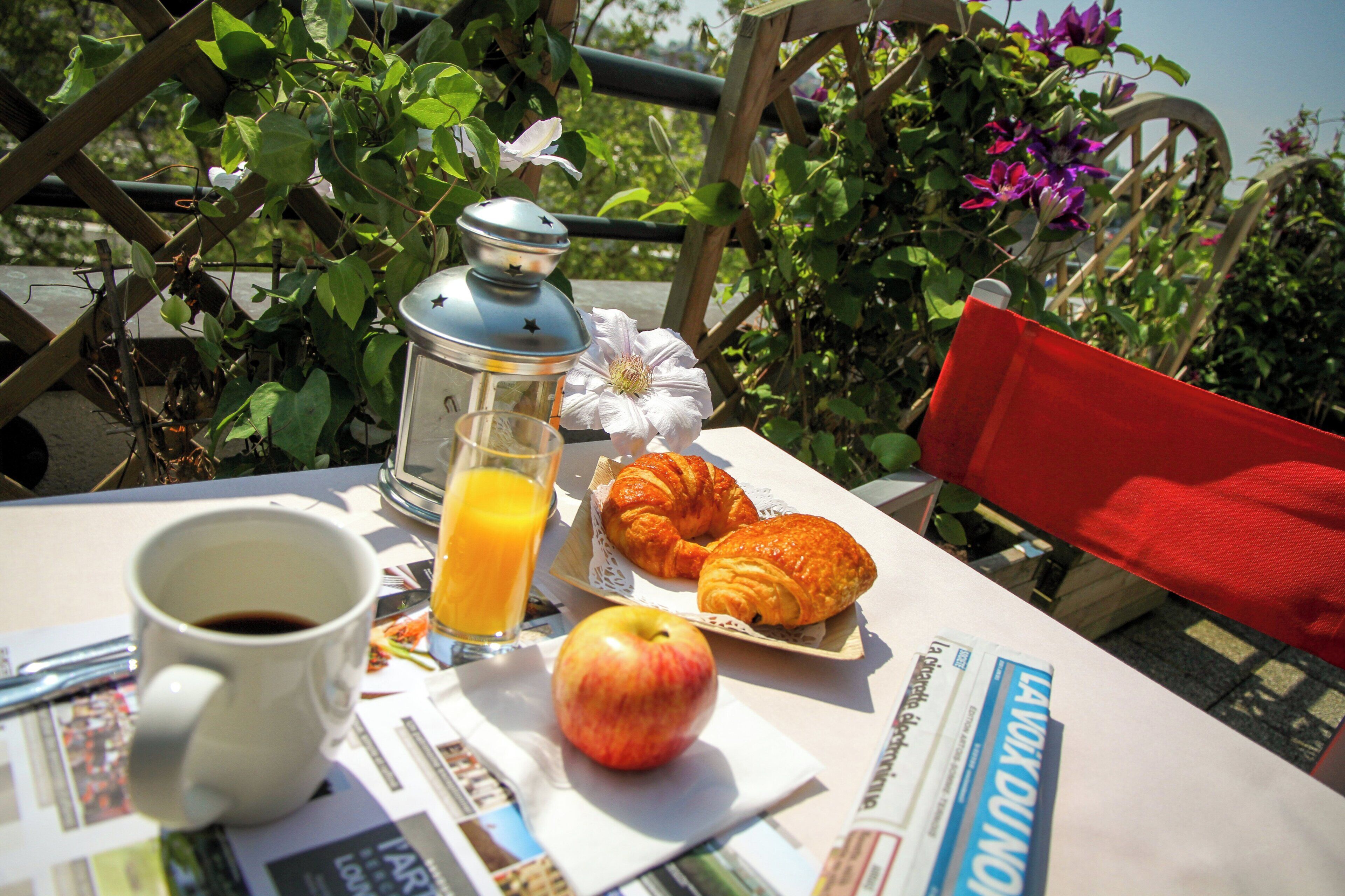 A table with a cup of coffee, a glass of orange juice, a plate with croissants, an apple, and a book.