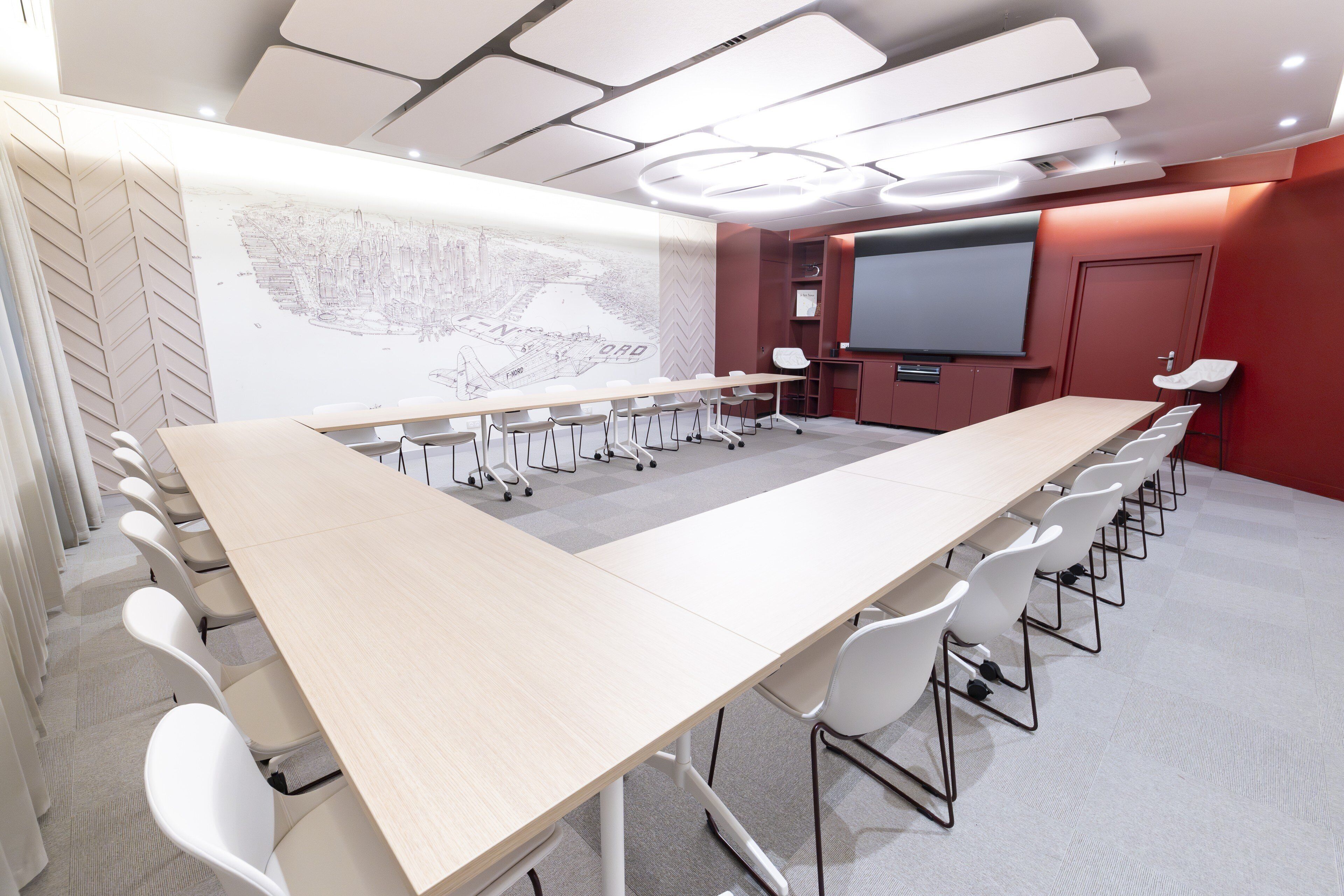 Un salón de conferencias con una larga mesa, sillas blancas, una pantalla grande y un mapa en la pared.