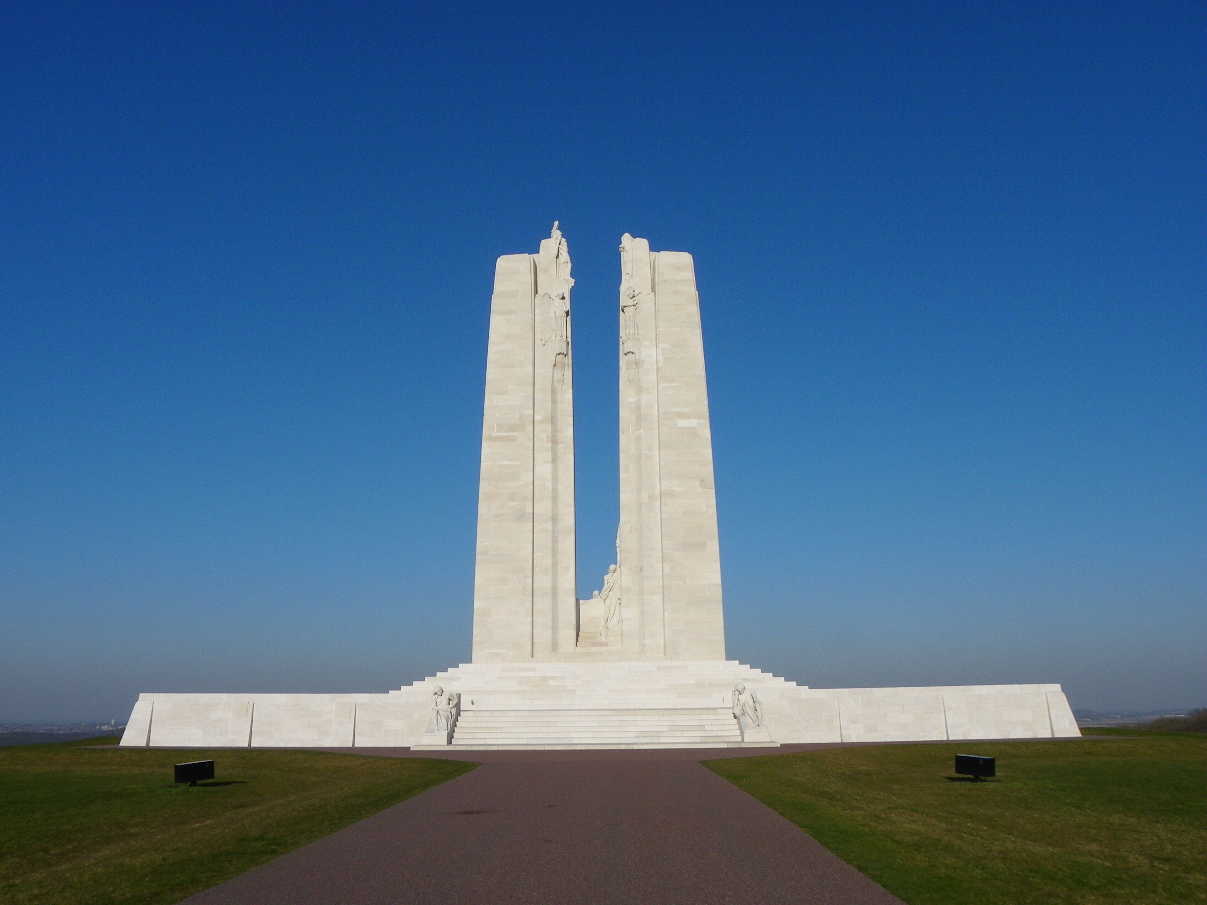A large white monument with two tall columns and a central statue, surrounded by a paved walkway and grassy areas.