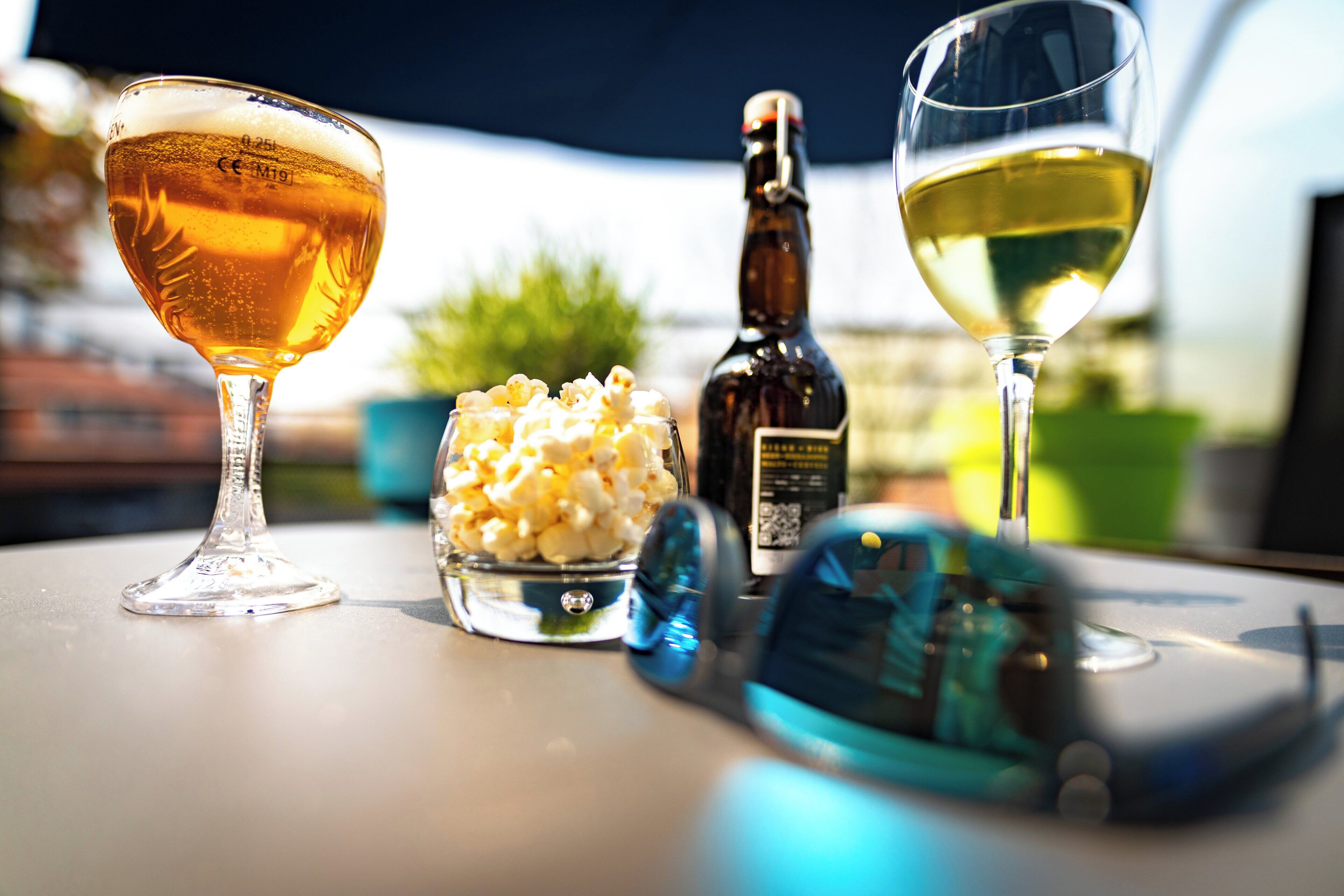 Un tavolo con due bicchieri di birra, una bottiglia di birra, una ciotola di popcorn e uno smartphone.