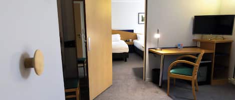 A hotel room with a bed, a desk, a chair, a television, and a door leading to another room.