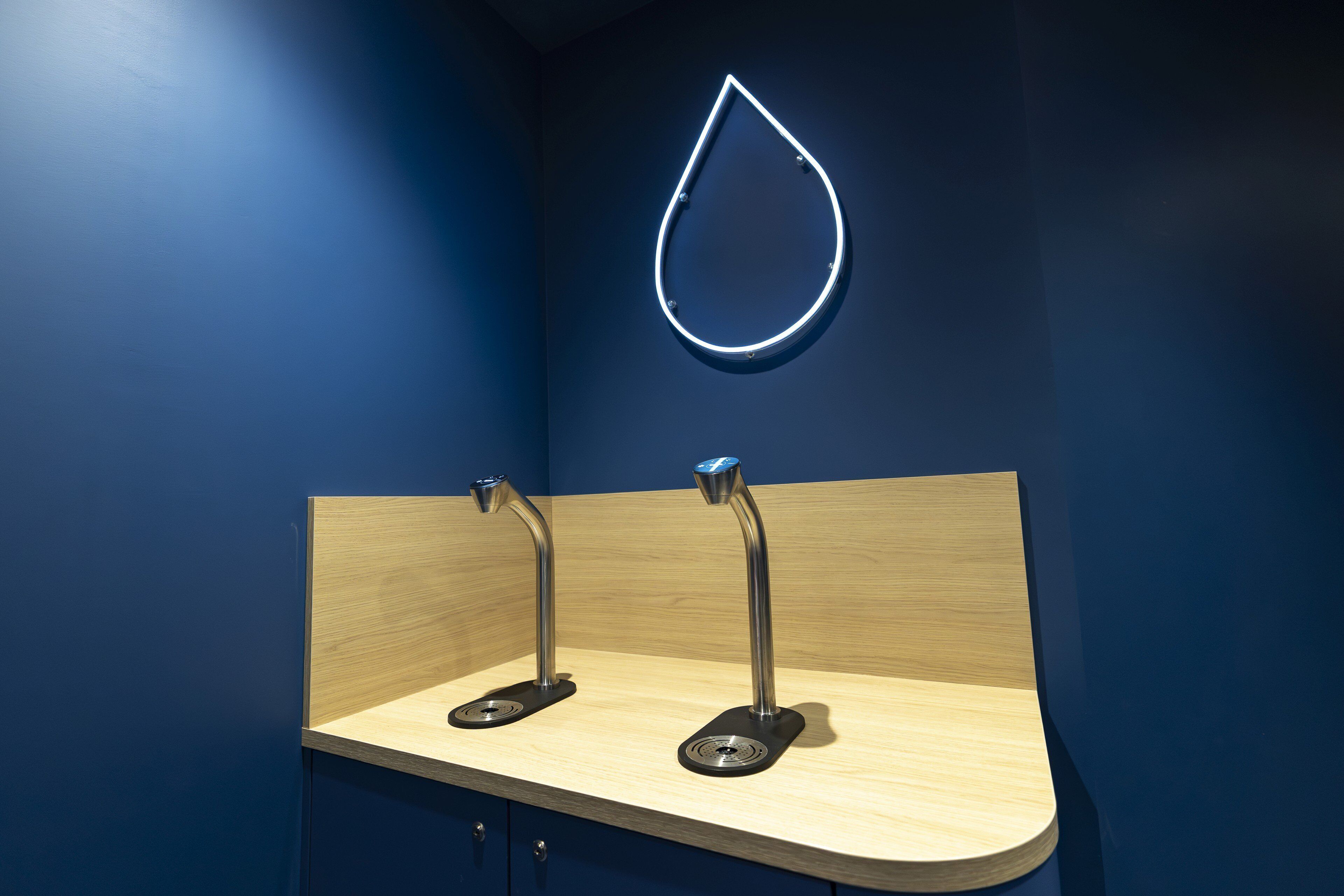 Un baño moderno con una pared azul oscuro, un mueble de tocador de madera y dos grifos metálicos.