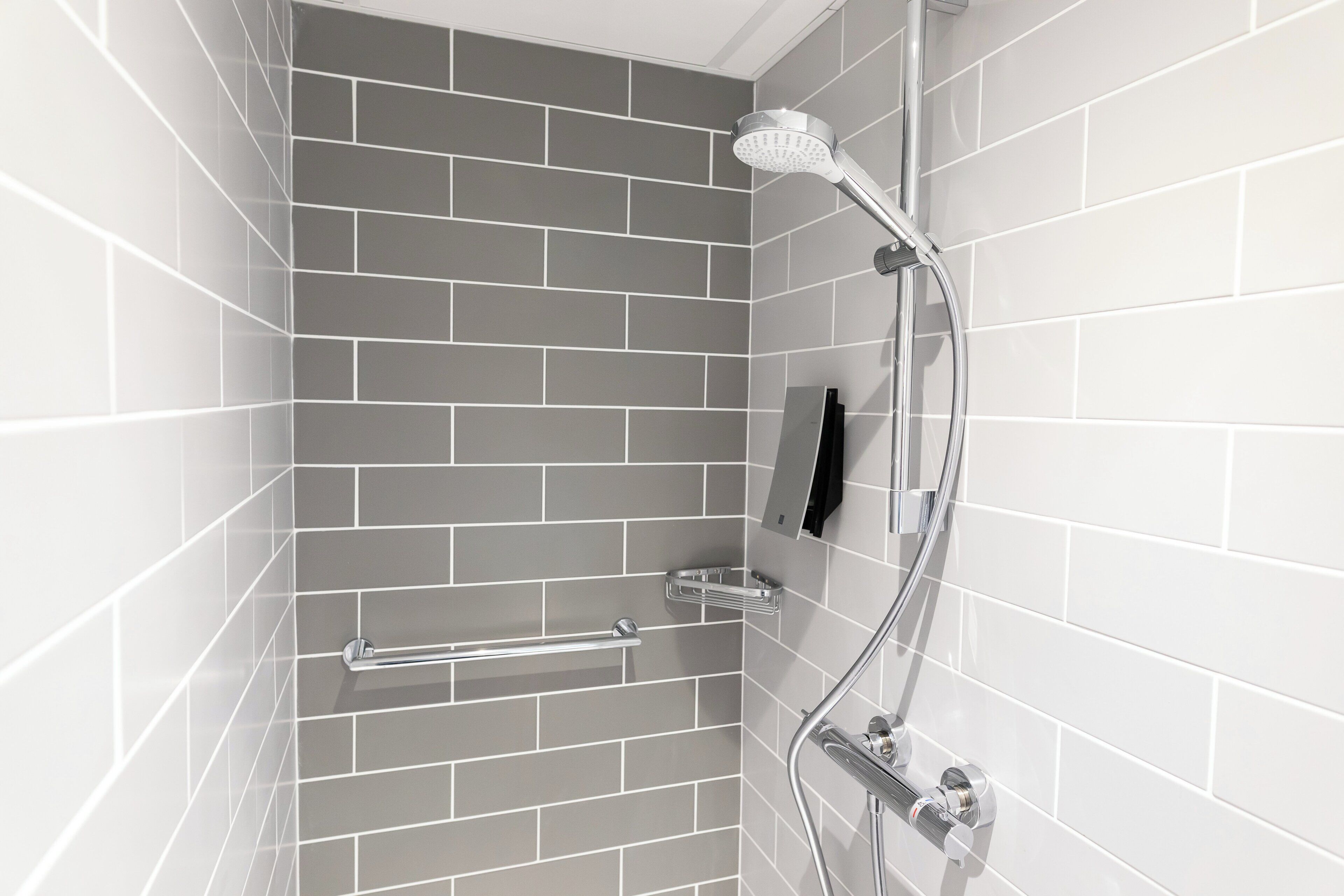 A shower with a handheld showerhead, a towel bar, and a soap dish on the wall.