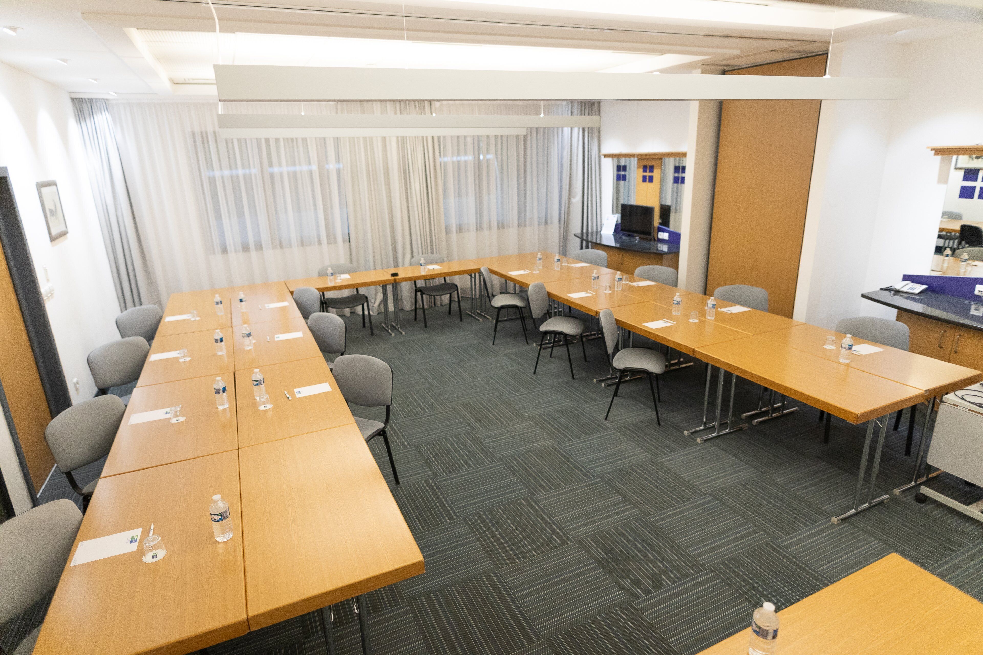 Une salle de conférence équipée de longues tables, de chaises et d’un petit coin cuisine.
