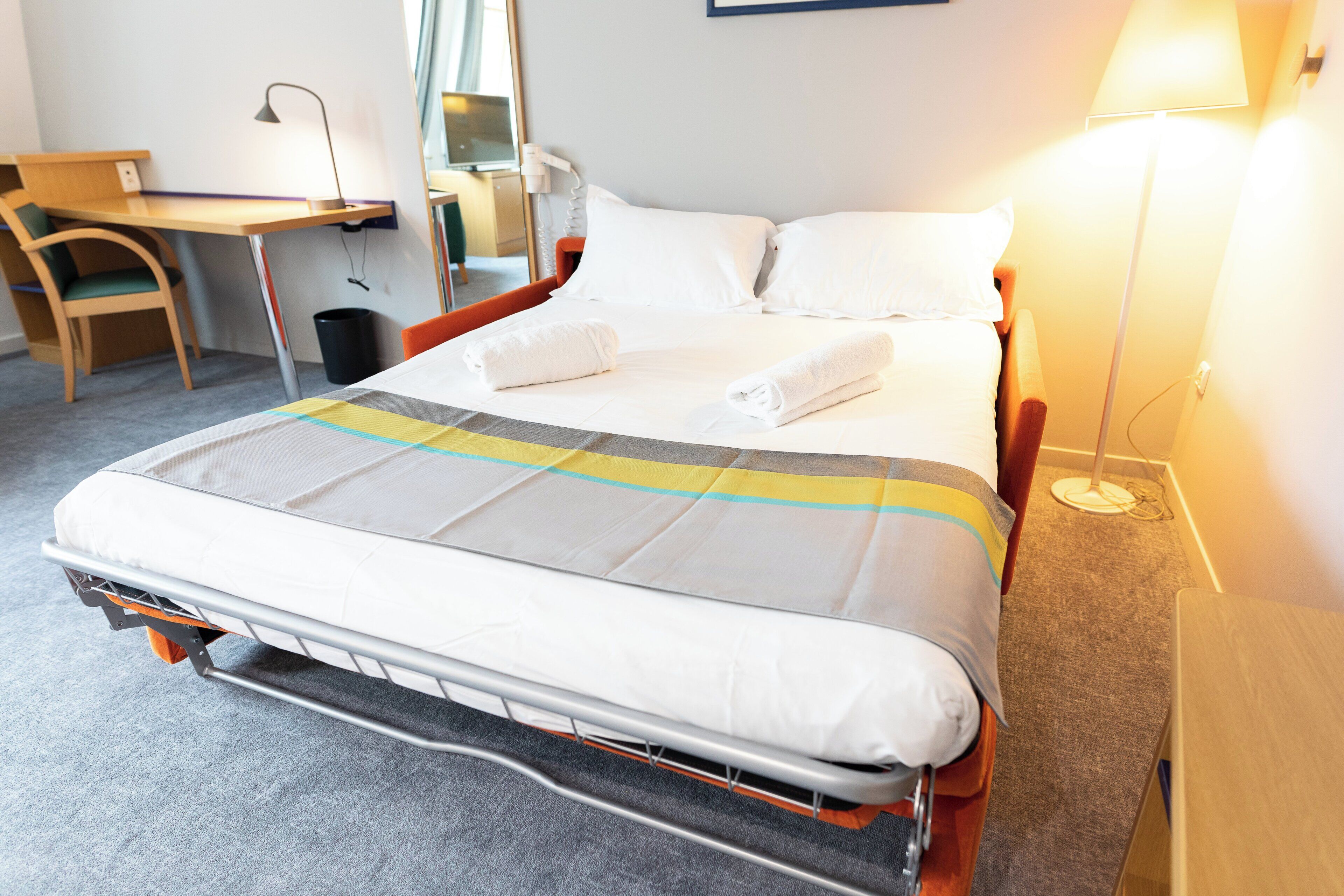 Una habitación de hotel con una cama, un escritorio, una silla, una lámpara y una mesita de noche.