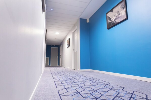 A hallway with a geometric patterned carpet, a blue wall, and a framed picture on the wall.