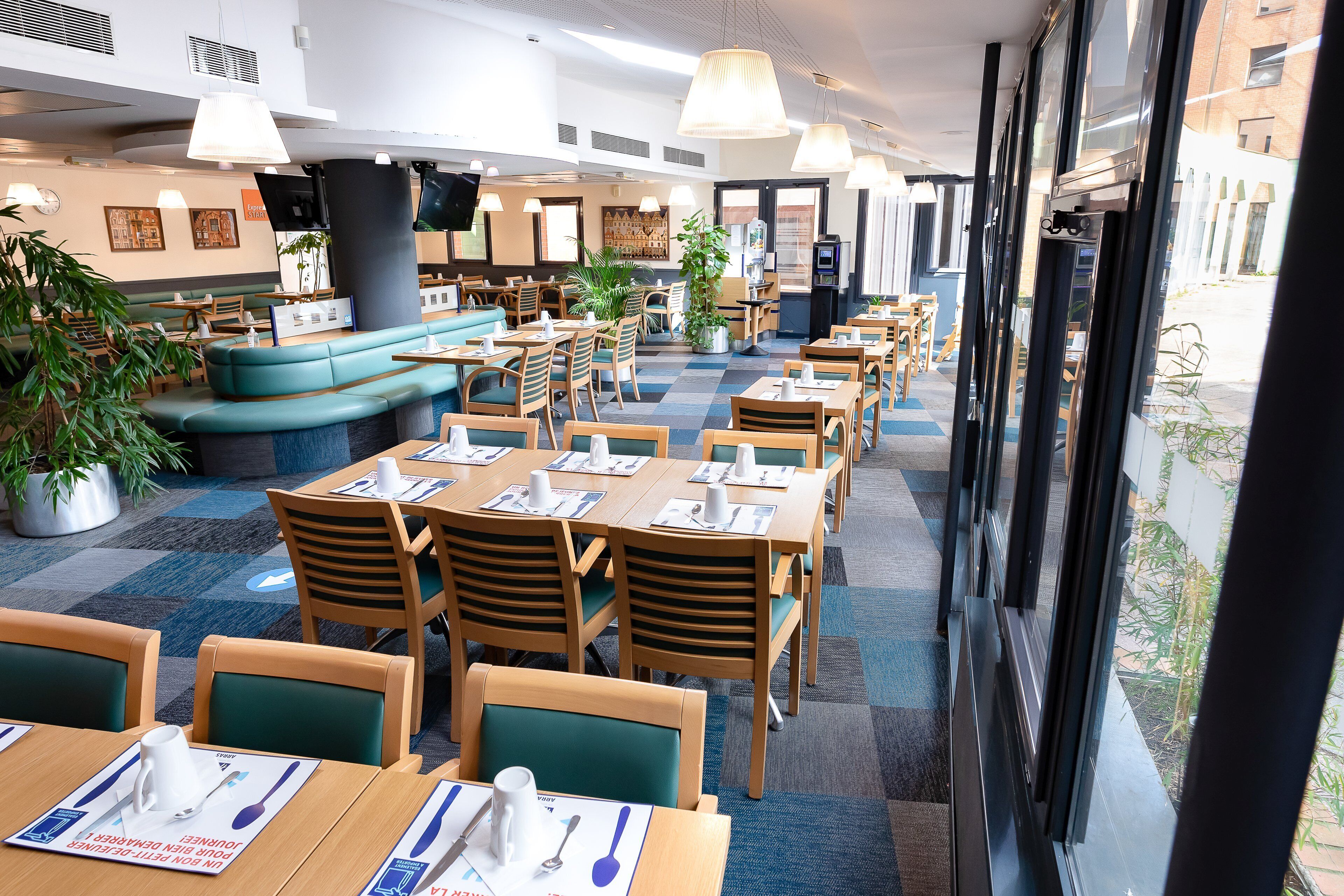 A restaurant with multiple dining tables and chairs, a seating area with a sofa, and potted plants.