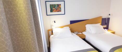 Une chambre d’hôtel avec deux lits, une table de chevet, une lampe et un tableau encadré au mur.