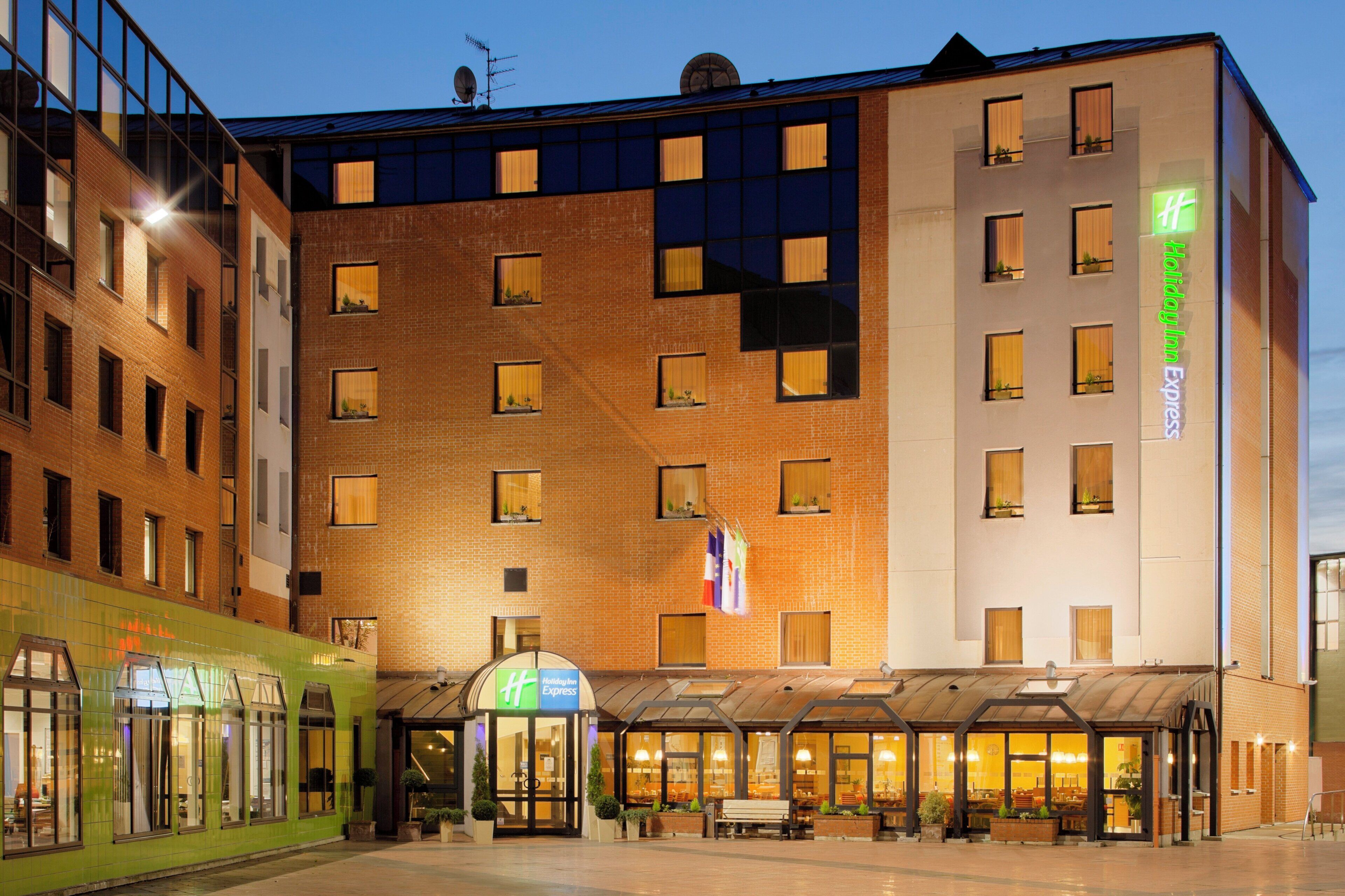 Un hotel Holiday Inn Express con fachada de ladrillo, múltiples ventanas y un área de estar exterior cubierta.