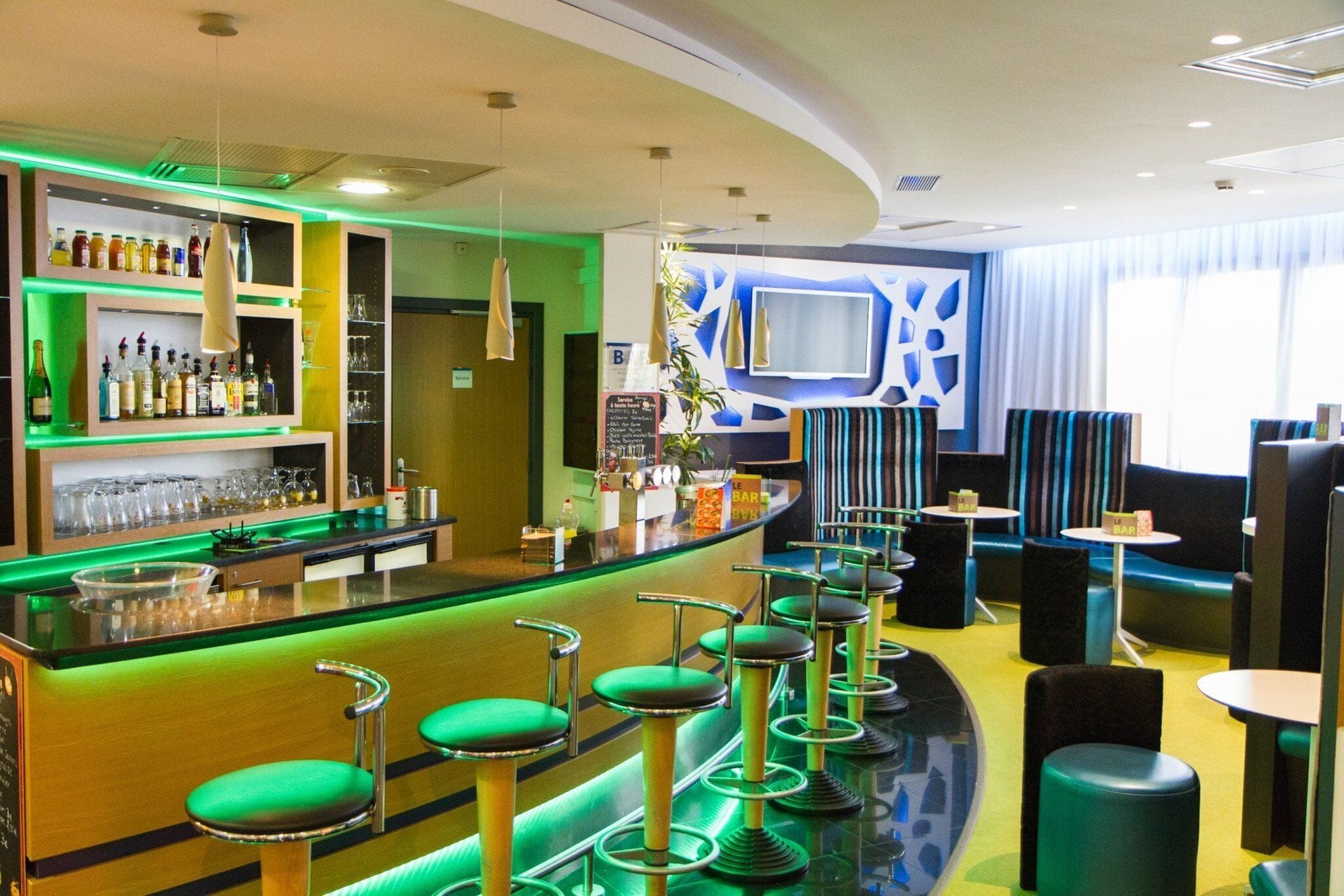 Een bar met krukken, een toonbank vol flessen en een aan de muur bevestigde televisie.