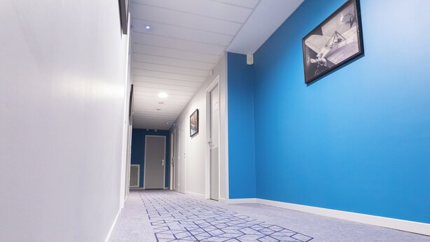 A hallway with a geometric patterned carpet, white walls, and a blue accent wall with a framed picture.