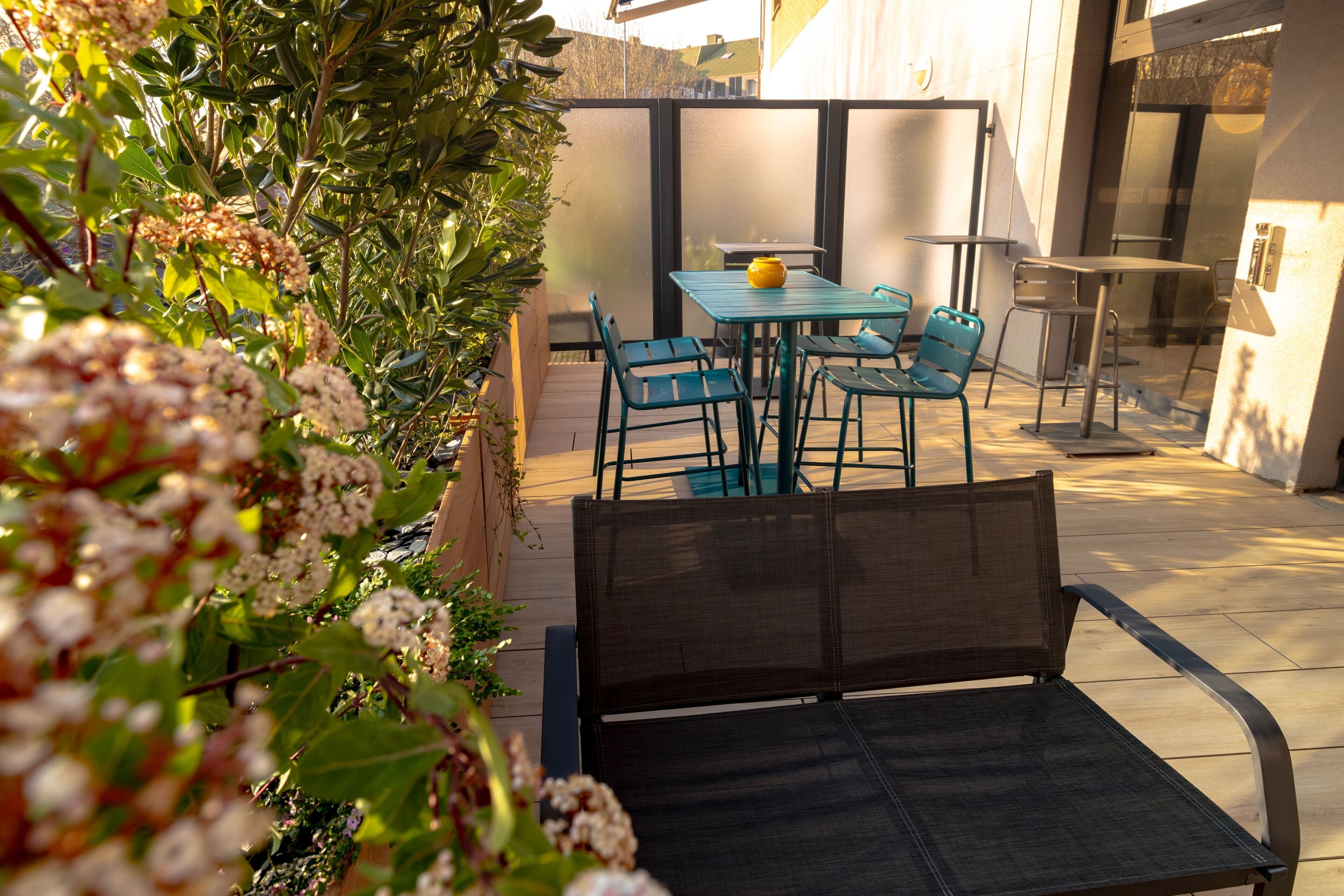 Une terrasse avec une table et des chaises, entourée de plantes et séparée par une paroi en verre.