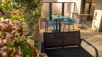 Une terrasse avec une table et des chaises, entourée de plantes et séparée par une paroi en verre.
