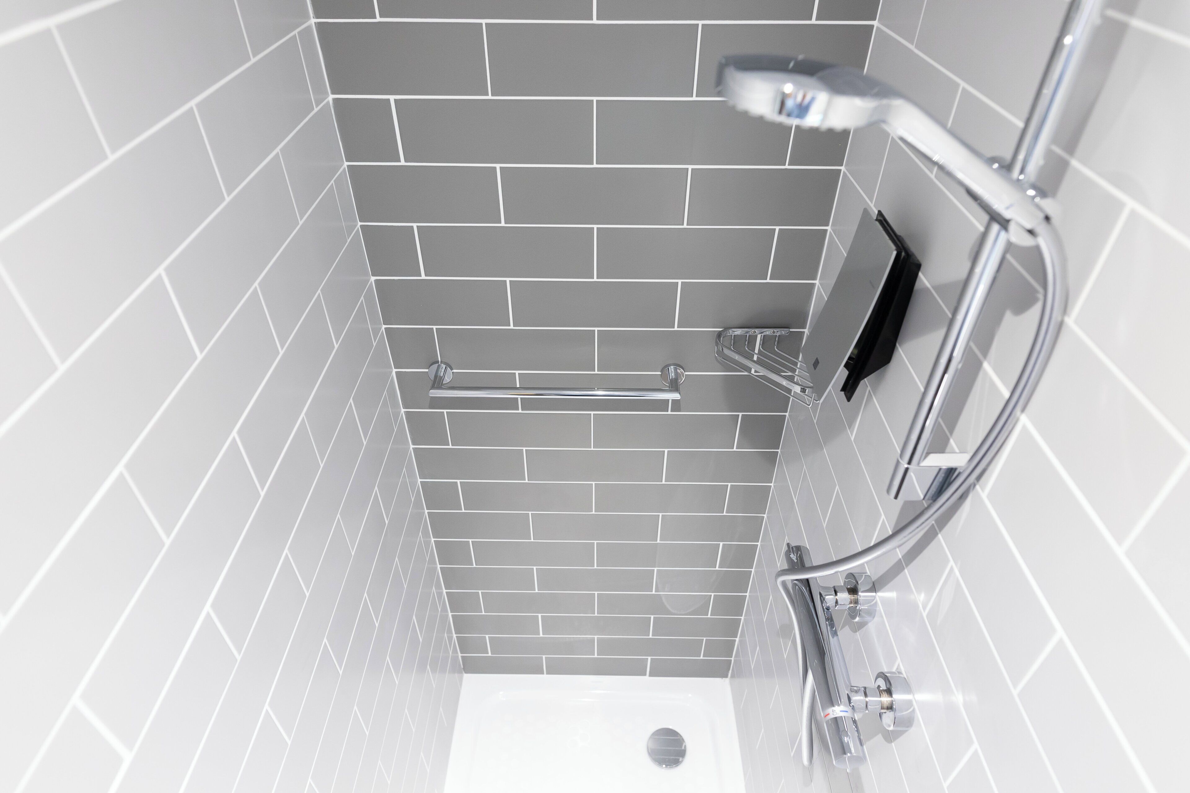 A modern bathroom with grey tiled walls, a chrome shower head, and a handheld shower.