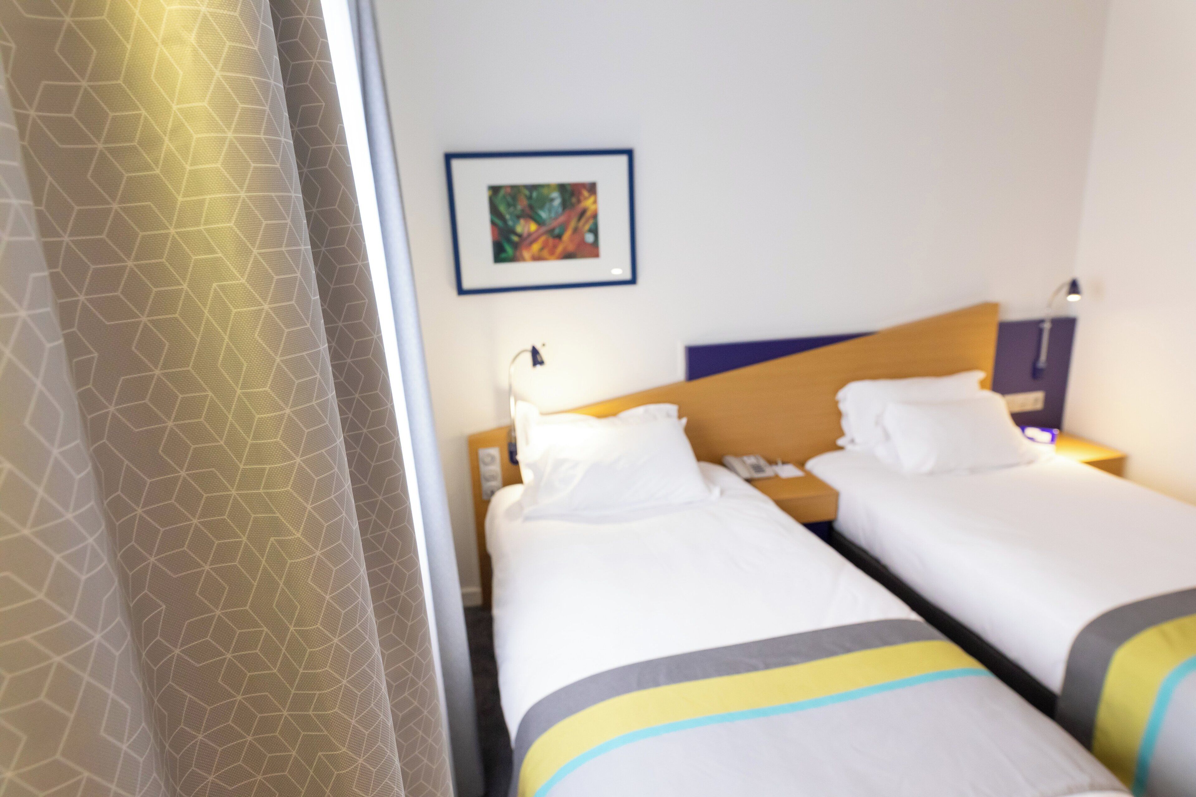 A hotel room with two beds, a nightstand, a lamp, and a framed picture on the wall.
