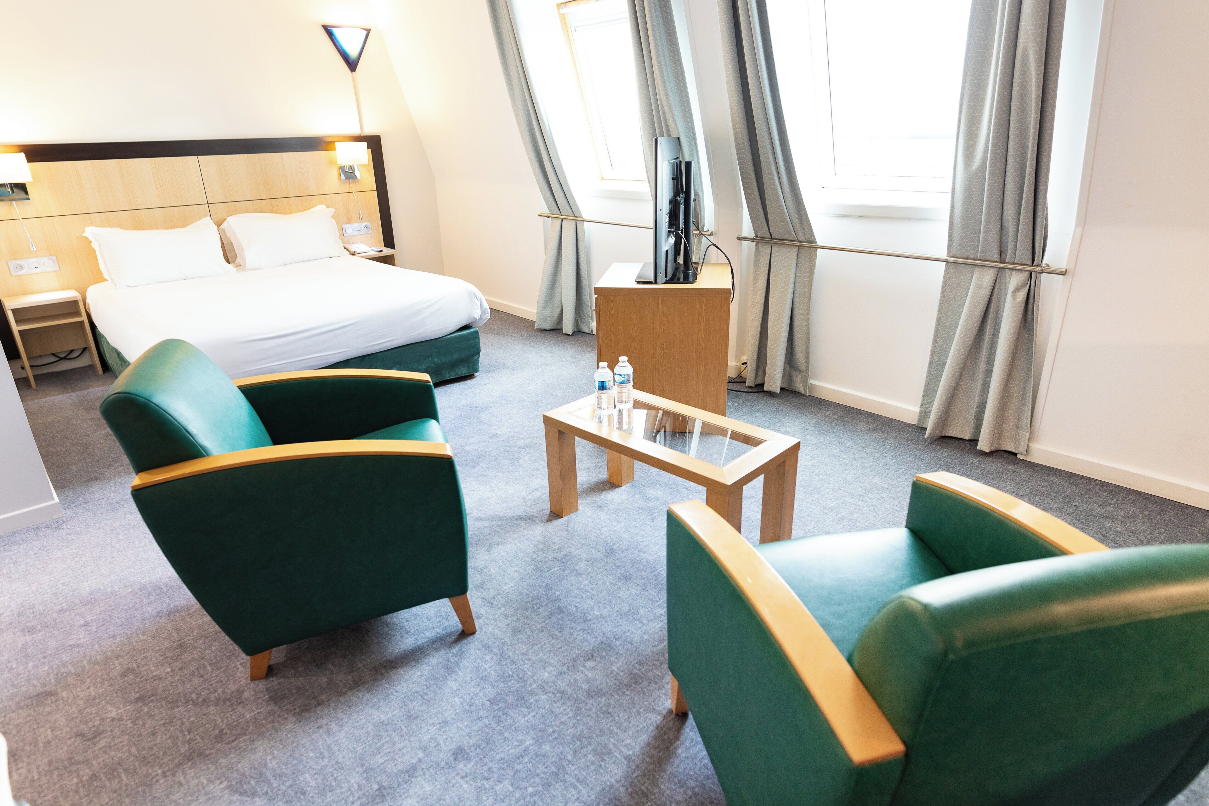Ett hotellrum med en säng, två fåtöljer, ett soffbord, en tv och ett fönster med gardiner.
