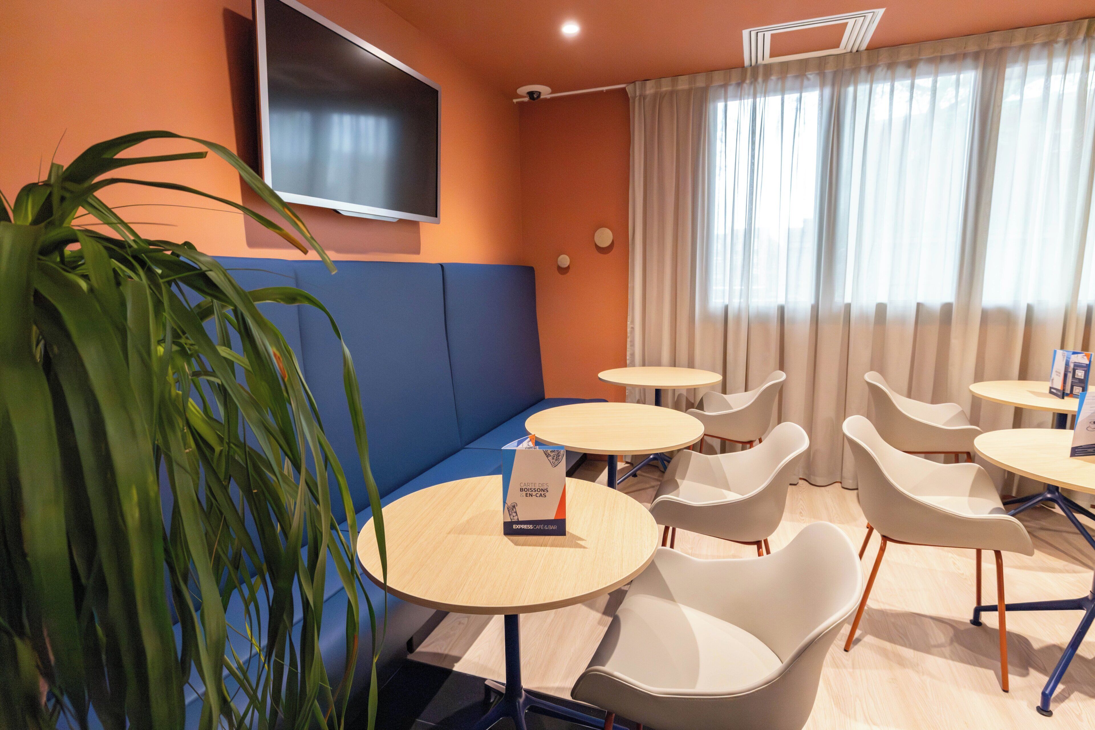 Une pièce moderne avec un banc bleu rembourré, des tables rondes et des chaises blanches.