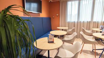 Une pièce moderne avec un banc bleu rembourré, des tables rondes et des chaises blanches.