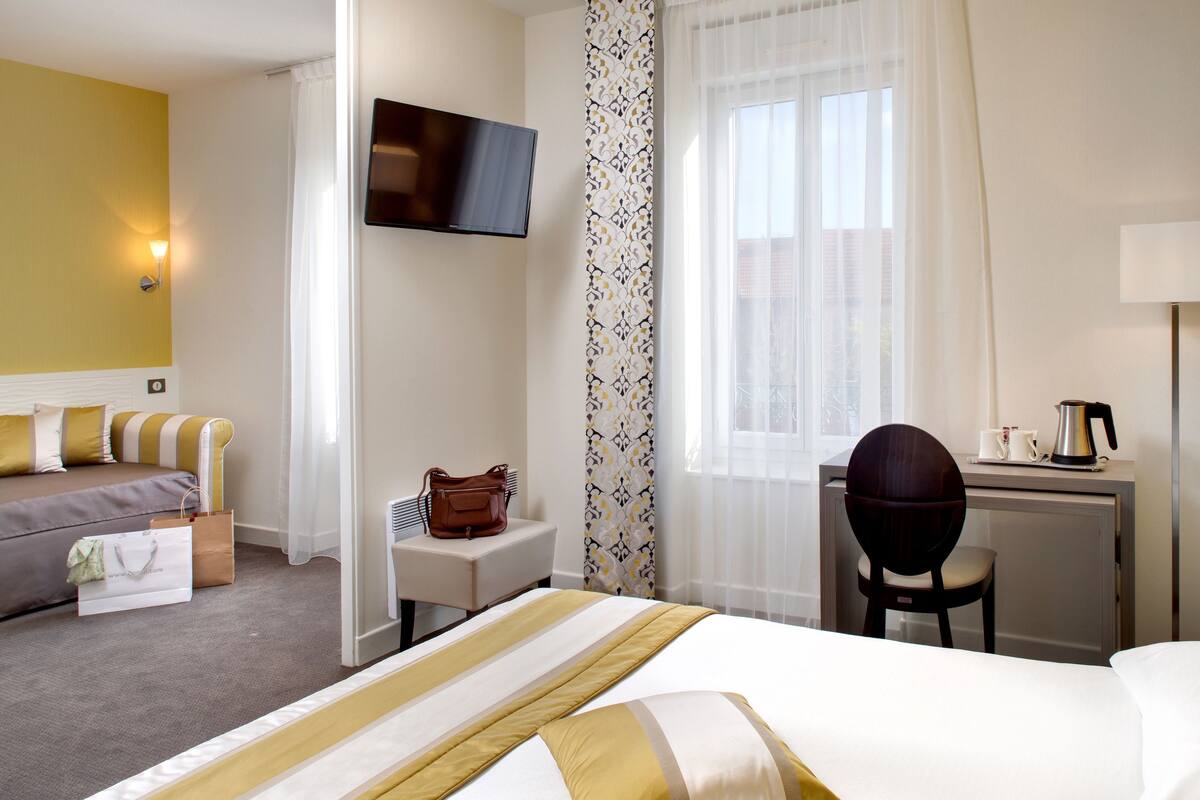 Una habitación de hotel con cama, escritorio, silla, televisor y ventana con cortinas.